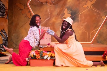 Two women clasp hands and smile during a scene in Honeypot
