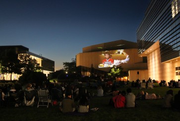 Summer Cinema attendees watch a movie on the Arts Green Lawn at dusk