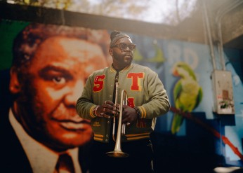 Marquis Hill holds a trumpet in front of a mural