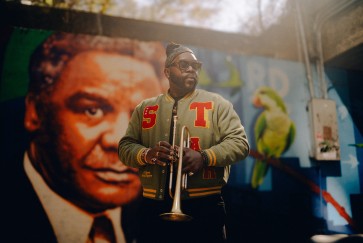 Marquis Hill holds a trumpet in front of a mural