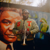 Marquis Hill holds a trumpet in front of a mural