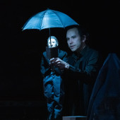 Puppeteer holding a man reading a book under an umbrella