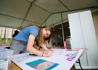 A student works on a posterboard for the Tabletop Club ahead of a previous org fair