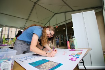 A student works on a posterboard for the Tabletop Club ahead of a previous org fair