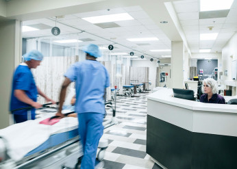 Two people in scrubs wheel a bed with a child in it down a hospital hallway