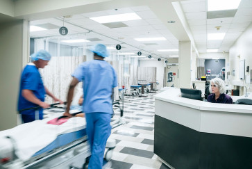 Two people in scrubs wheel a bed with a child in it down a hospital hallway