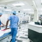 Two people in scrubs wheel a bed with a child in it down a hospital hallway