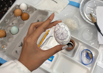 a hand holds an in-progress pysanky egg with a design in pencil on it