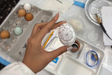 a hand holds an in-progress pysanky egg with a design in pencil on it