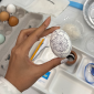 a hand holds an in-progress pysanky egg with a design in pencil on it