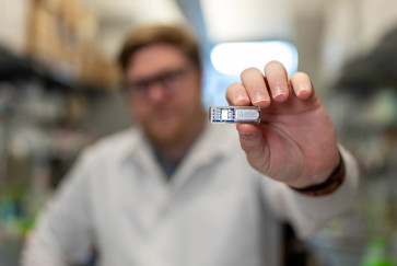 A man in a lab coat holds up the small rectangular HOBIT device