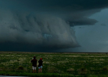Two people stand in a field taking photos of gathering storm clouds