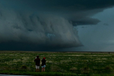 Two people stand in a field taking photos of gathering storm clouds