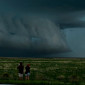Two people stand in a field taking photos of gathering storm clouds