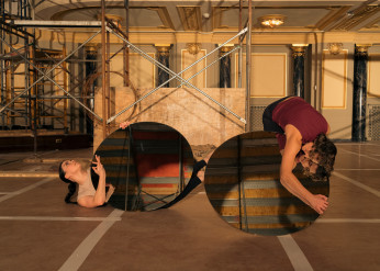 Three dancers onstage at the Driehaus Museum, two hold circular mirrors reflecting the space