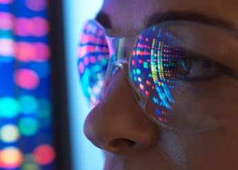 A close up of the eyes of a woman wearing safety glasses looking at a screen