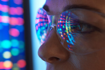 A close up of the eyes of a woman wearing safety glasses looking at a screen