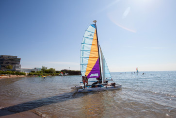Five people push a catamaran off the beach at the sailing center