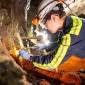a woman in reflective gear and a hard hat chisels at a rock wall