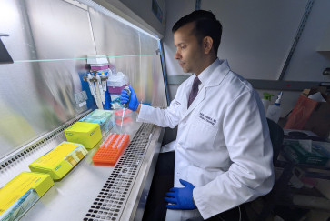 A man in a white coat works at a lab bench