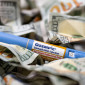 A blue Ozempic GLP-1 autoinjector sits in a pile of crumpled $100 bills