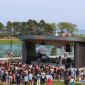 A crowd gathers in front of Kahn Pavilion, where a rock band plays, with the lagoon and Lake Michigan in the background