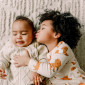 A baby lying on a blanket receives a kiss from an older sibling