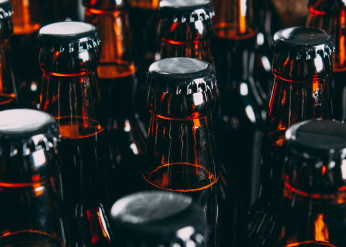A sea of the tops of brown glass bottles of beer, filled with liquid and capped with black metal