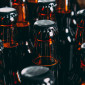 A sea of the tops of brown glass bottles of beer, filled with liquid and capped with black metal