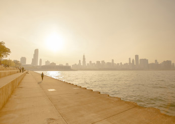 People walk along a concrete walkway by Lake Michigan with the Chicago skyline in the background