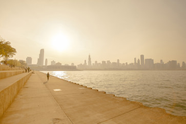 People walk along a concrete walkway by Lake Michigan with the Chicago skyline in the background