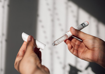 A left hand holds the cap of an autoinjector while the right holds the corresponding body of the device
