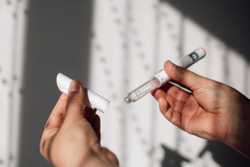 A left hand holds the cap of an autoinjector while the right holds the corresponding body of the device