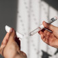 A left hand holds the cap of an autoinjector while the right holds the corresponding body of the device