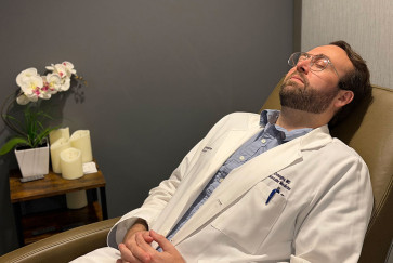 A doctor in a white coat lays back in a chair