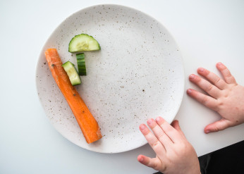 a child's hands next to a plate with a carrot stick and cucumber slices