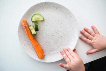 a child's hands next to a plate with a carrot stick and cucumber slices