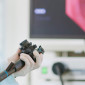 A gloved hands holds the controls of a scope for a colonscopy with a computer screen in the background