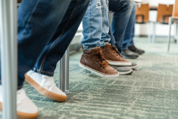 The legs of three people sitting in a waiting room, the middle pair don't touch the ground