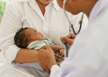 A mother holds a baby while a doctor uses a stethoscope