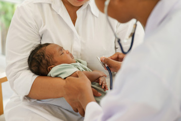 A mother holds a baby while a doctor uses a stethoscope