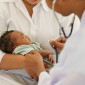A mother holds a baby while a doctor uses a stethoscope