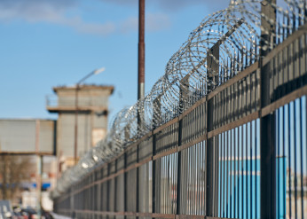 a metal fence topped with barbed wire, with a building and watchtower in the background