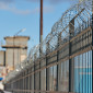 a metal fence topped with barbed wire, with a building and watchtower in the background