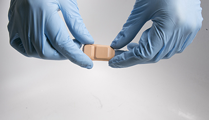 Blue-gloved hands holding bandage-like sensor
